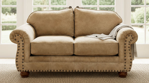 Sofá beige con ribete de tachuelas en una habitación con grandes ventanas.