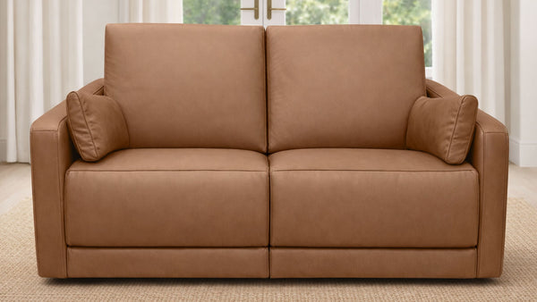 Sofá de cuero marrón con cojines en una habitación con cortinas y una ventana.