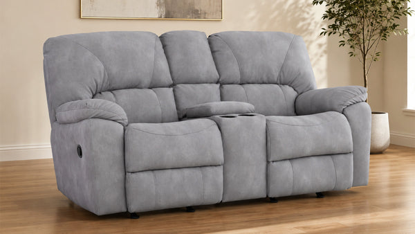 A gray three-seat reclining loveseat with a center console cup holder, shown in a staged living room setting with wood floors and a potted plant.