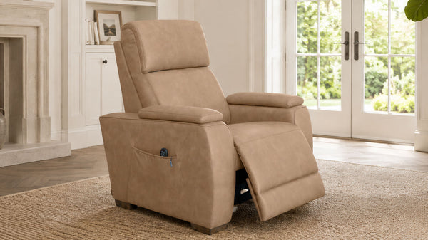 A beige upholstered recliner chair shown in a bright living room with a window, fireplace, and rug.
