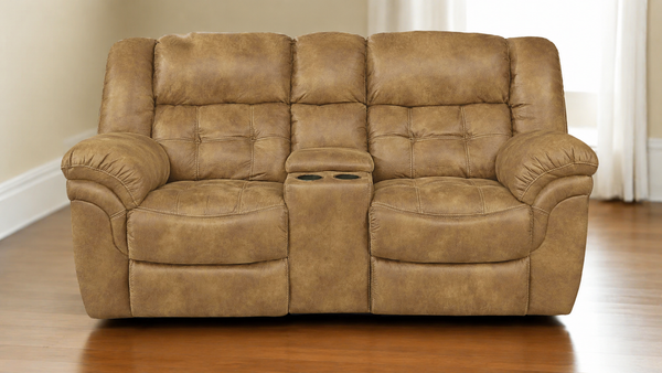 A brown tufted reclining loveseat with a center console and two cup holders, shown in a living room setting with wood floors and white curtains.