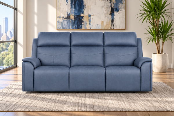 Un sofá reclinable de tres plazas de cuero azul, situado sobre una alfombra beige con textura, en un salón de estilo moderno con una ventana, vistas a la ciudad y una planta en maceta.