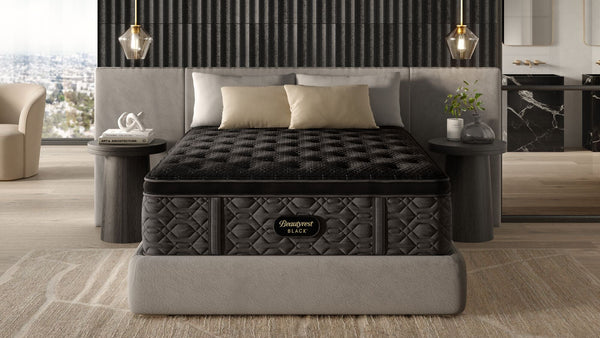 Un colchón Beautyrest Black Series 3 Medium Pillowtop de tamaño queen expuesto en un dormitorio moderno con una almohada sobre la cama, una mesita de noche y una gran ventana.