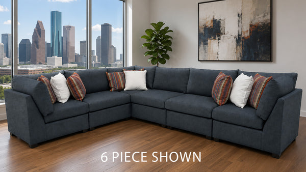 A 6-piece sectional sofa in a dark slate blue-gray fabric, styled with white and striped accent pillows in a modern living room with a city skyline view.