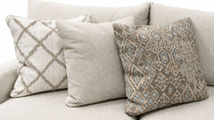 Three decorative throw pillows arranged on a light beige sofa. The center pillow is a solid light beige linen texture, flanked by two patterned pillows in beige, taupe, and light blue-gray tones.