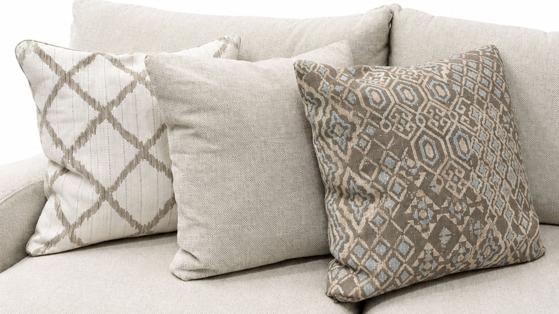 Three decorative throw pillows arranged on a light beige sofa. The center pillow is a solid light beige linen texture, flanked by two patterned pillows in beige, taupe, and light blue-gray tones.