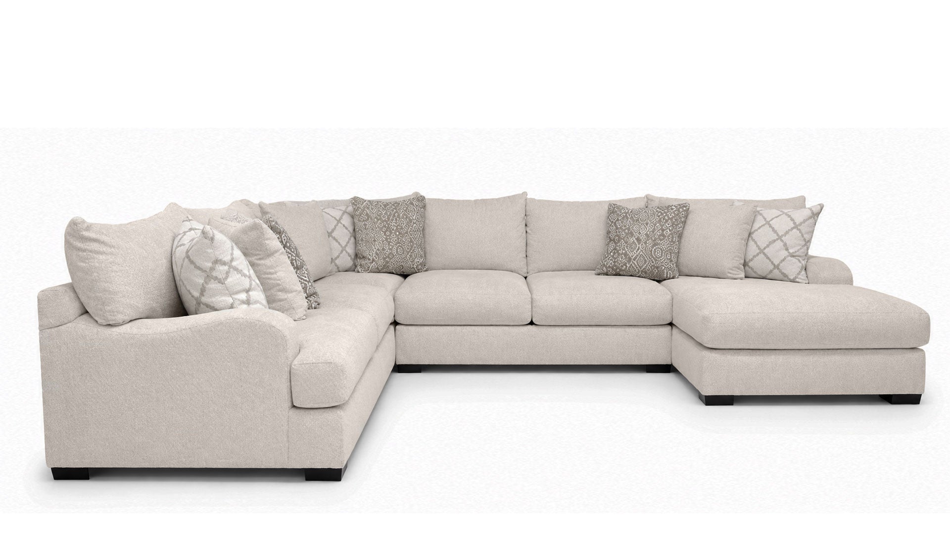 A light beige fabric sectional sofa with a chaise lounge on the right side, styled with multiple throw pillows in neutral tones, set against a plain white background.