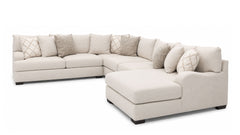 A light beige fabric sectional sofa with a right-facing chaise lounge, styled with multiple decorative throw pillows in neutral tones, shown against a solid white background.