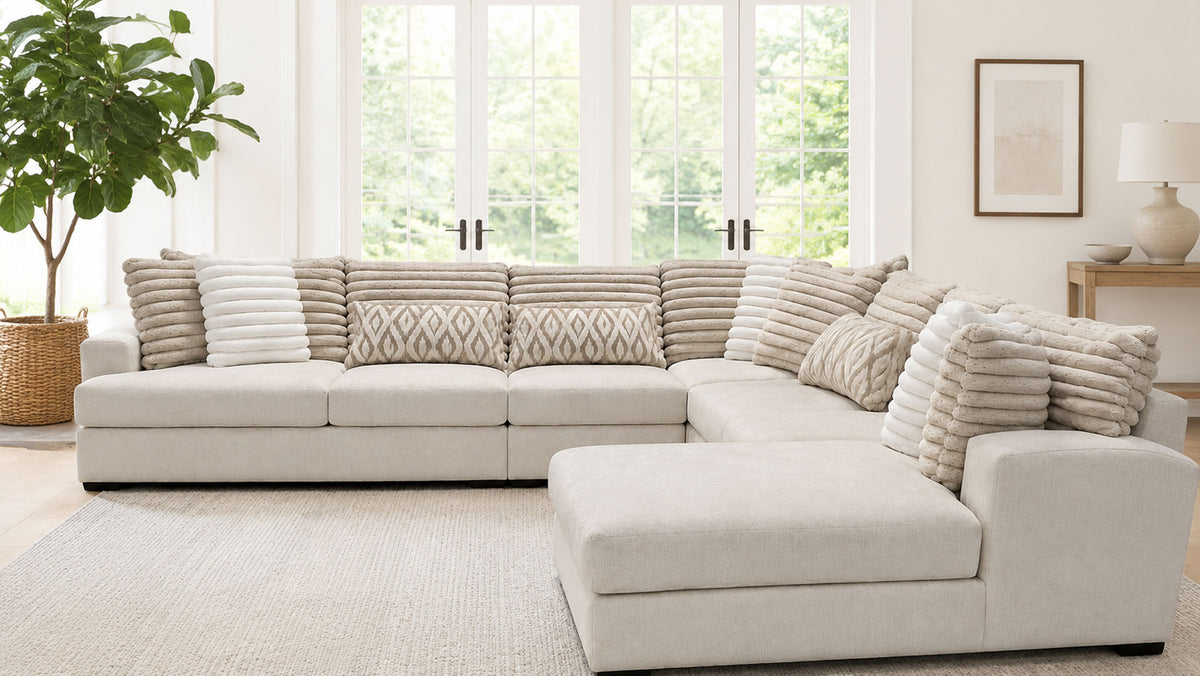 Beige sectional sofa in a living room with large windows and a plant.