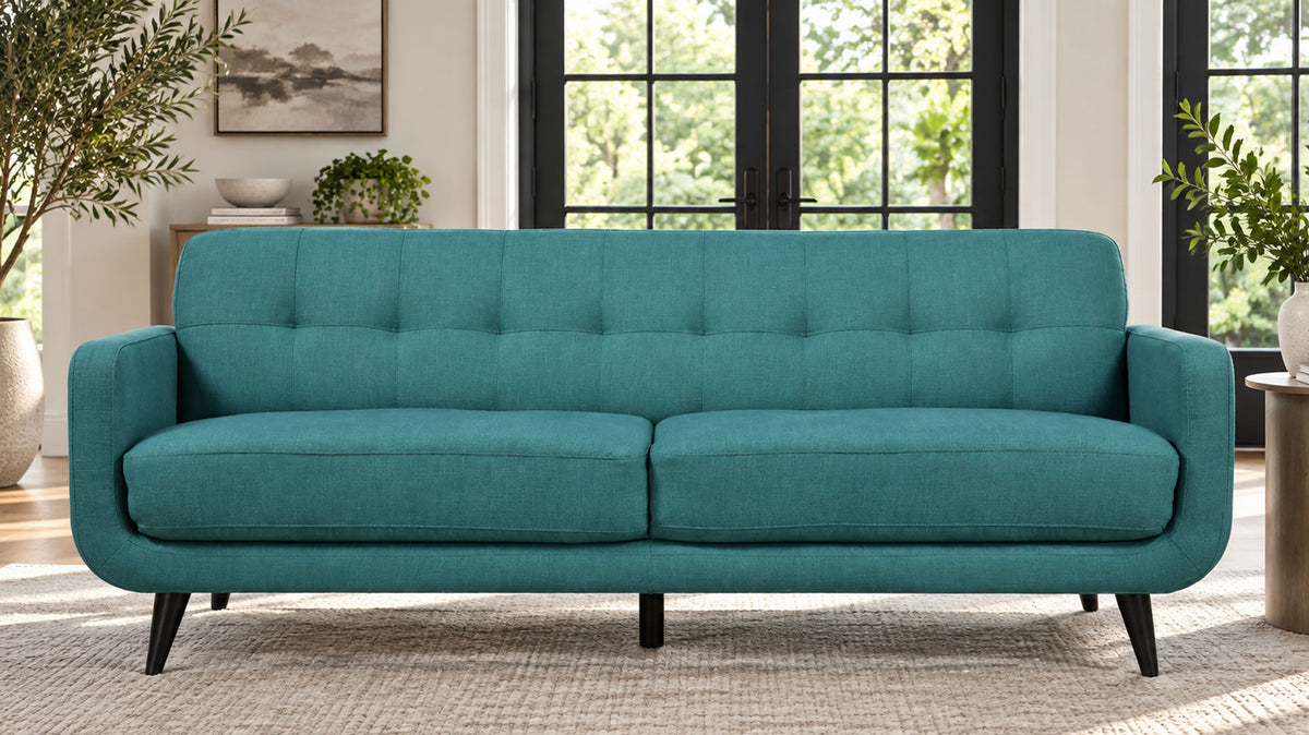 A teal blue-green upholstered loveseat with tufted back cushions and tapered black legs, shown in a bright living room setting.
