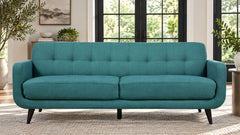 A teal blue-green upholstered loveseat with tufted back cushions and tapered black legs, shown in a bright living room setting.