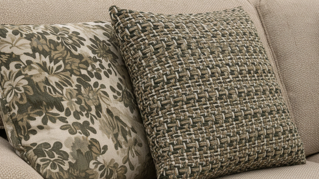 Two decorative pillows on a sofa with one having a floral pattern and the other a woven texture.