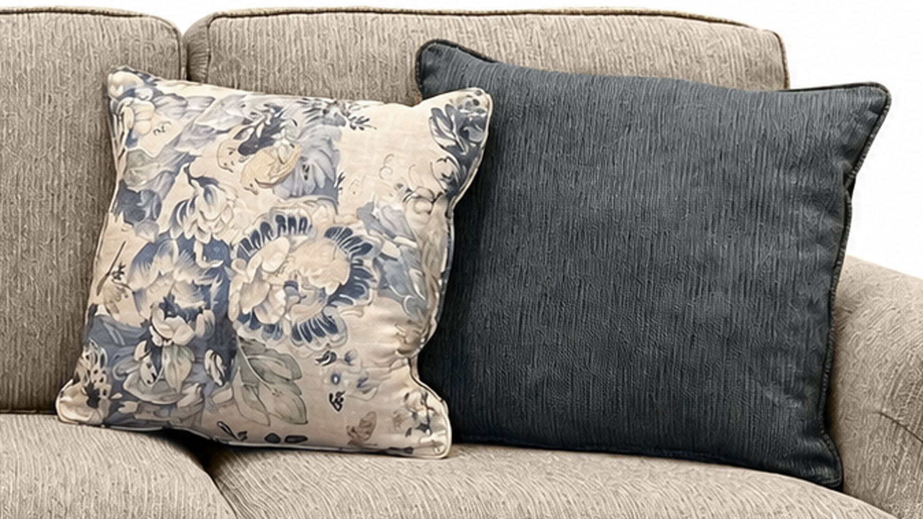 Two decorative pillows on a gray sofa, one floral and one solid color.