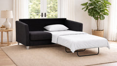 Black sofa bed with white mattress in a room with a plant and window.
