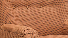 Close-up of a tufted upholstered armchair in a warm tan or camel fabric with a dense small-dot pattern and button tufting.