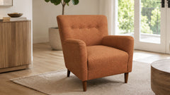 An orange textured armchair with button tufting on the backrest and tapered wooden legs, set in a bright, modern living room with light wood floors, a beige rug, and a glass door in the background.