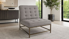 A modern tufted lounge chair with a light gray upholstered seat and backrest on a slim bronze metal frame, shown in a bright contemporary living room setting.