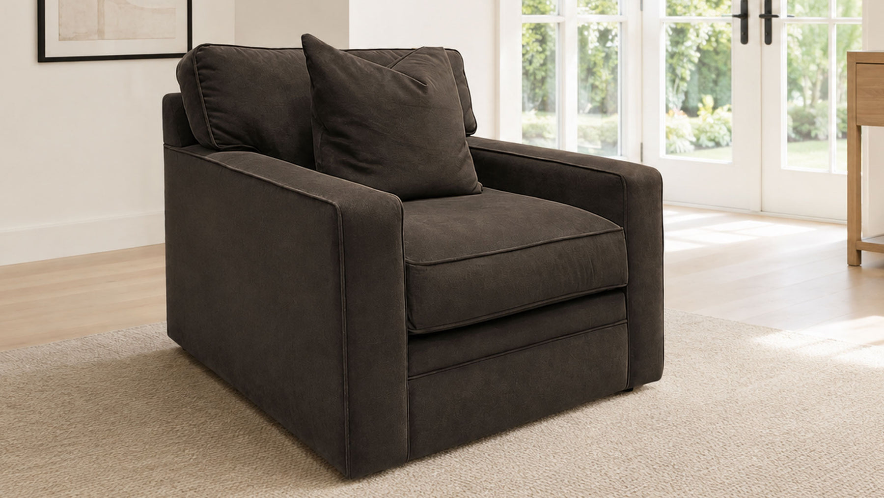 A dark brown upholstered armchair with a matching throw pillow, positioned on a beige carpet in a bright, modern living room with large windows.