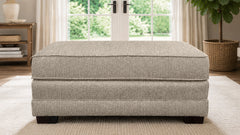 Gray upholstered ottoman in a room with a window and plant