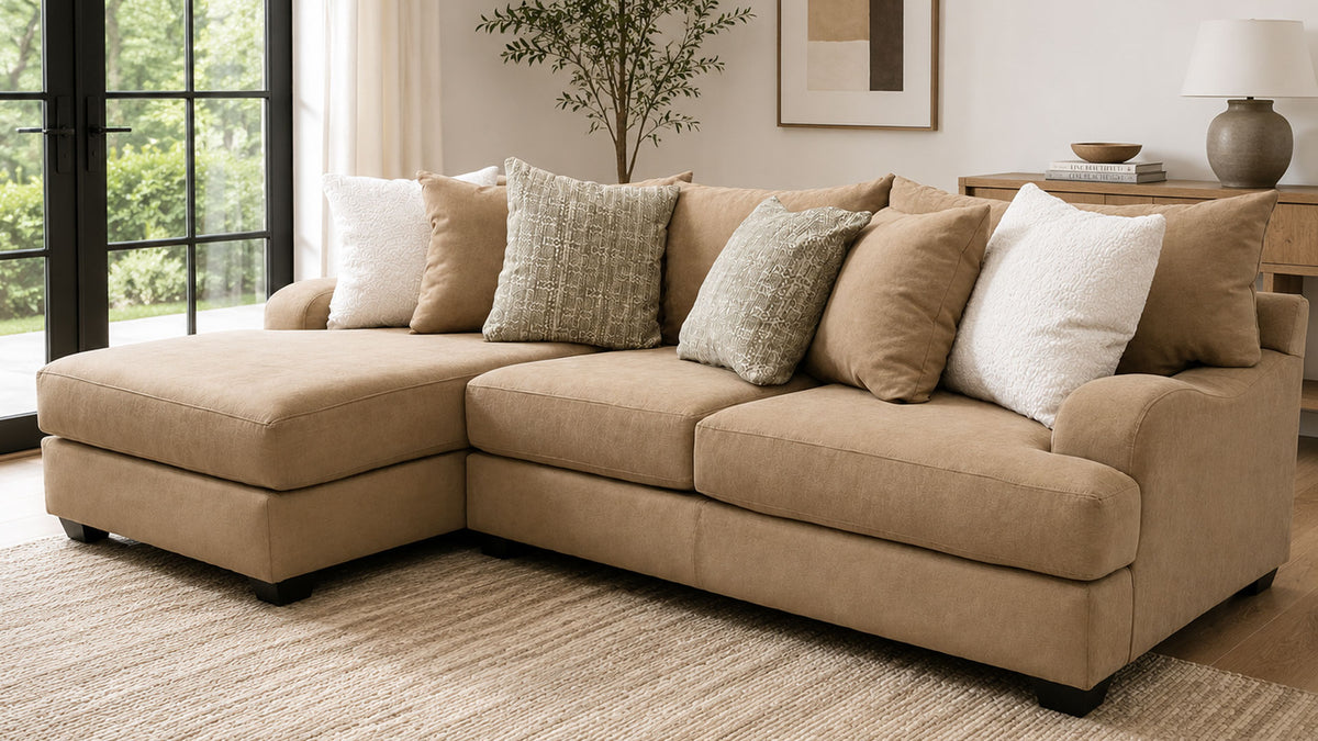 A beige sectional sofa with a left-facing chaise lounge, styled with multiple textured throw pillows in a bright, modern living room setting.