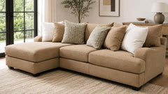 A beige sectional sofa with a left-facing chaise lounge, styled with multiple textured throw pillows in a bright, modern living room setting.