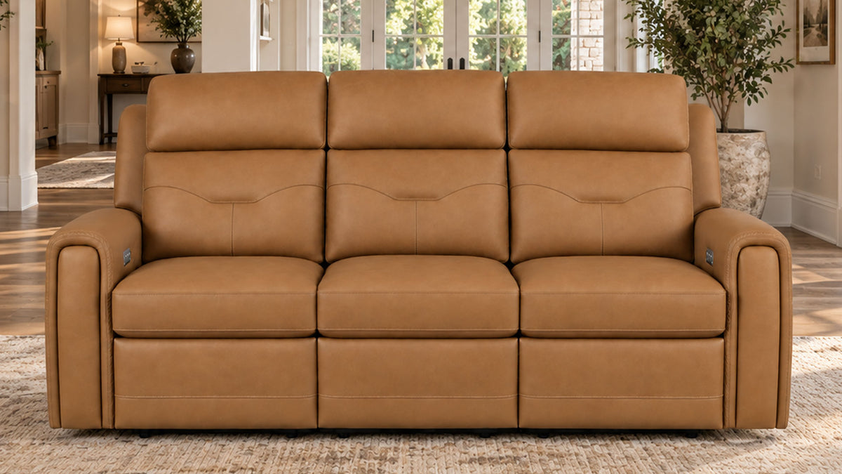 A three-seat power reclining leather sofa in tan brown, positioned on a textured area rug inside a bright, modern living room.