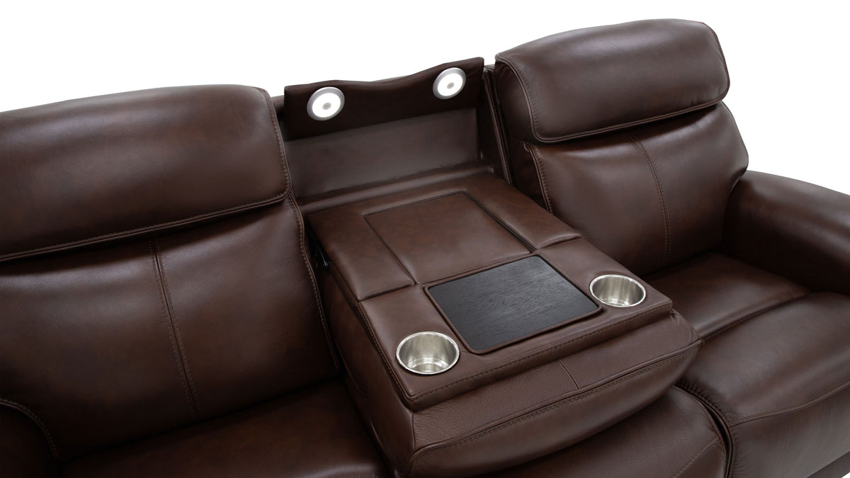 A close-up of a brown leather reclining sofa with a center console table featuring two cup holders and a black rectangular insert, shown against a white background.