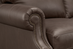 Primer plano de un sillón de cuero marrón con ribete decorativo de tachuelas.