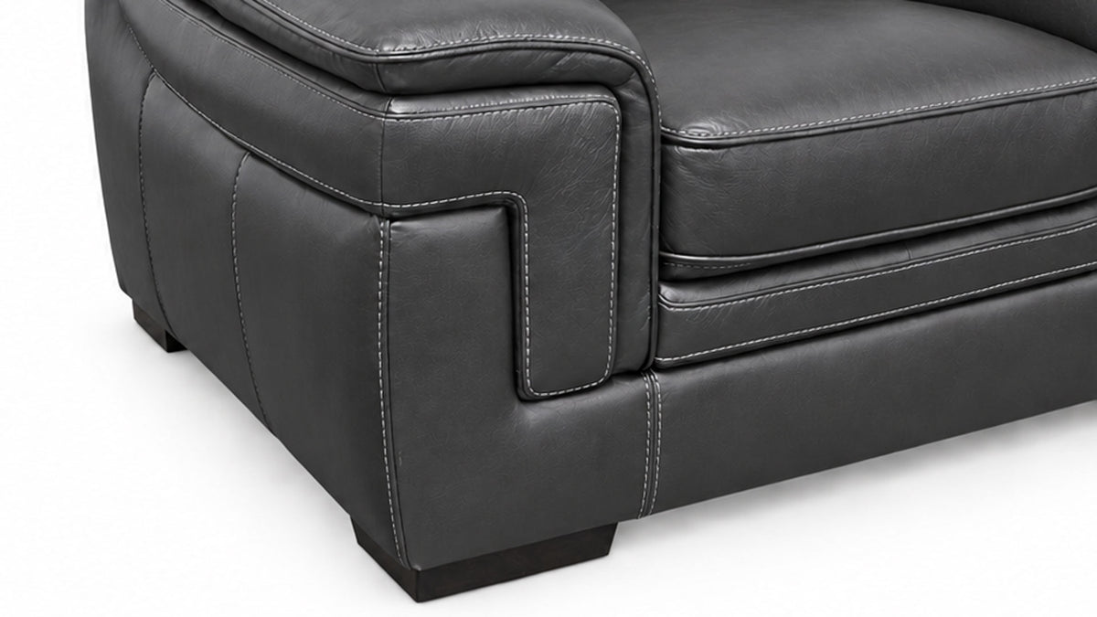 Close-up of a dark gray leather armchair showing the side bolster, channel tufting, and clean stitching on a white background.