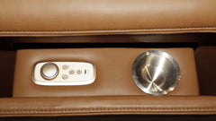 Close-up of a brown leather reclining chair feature, showing a built-in control panel with a rotary dial and buttons on the left and a stainless steel cup holder on the right.
