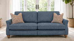A two-seater loveseat sofa upholstered in textured blue fabric, styled with two patterned throw pillows and wooden legs, set in a bright living room with a window and potted plant in the background.