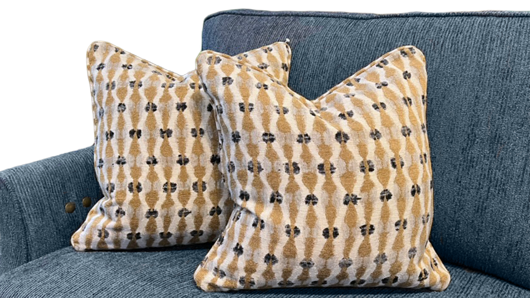 Two decorative throw pillows with a tan and cream ikat pattern featuring small black motifs, displayed on a textured blue-gray sofa.