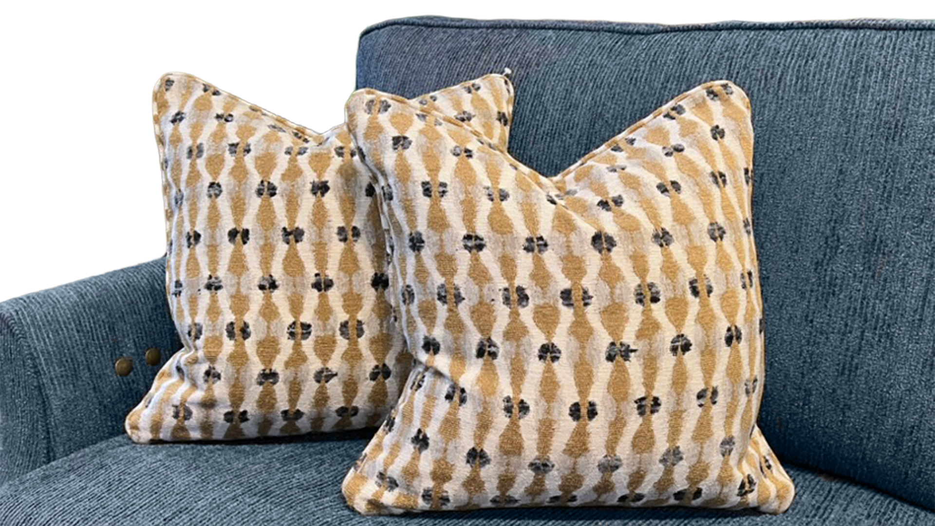 Two decorative throw pillows with a tan and cream ikat pattern featuring small black motifs, displayed on a textured blue-gray sofa.
