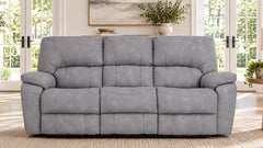 Un sofá de dos plazas reclinable, de color gris y con tres asientos, con cojines mullidos y capitoné, que se muestra en un salón luminoso con grandes ventanales y una alfombra de tonos neutros.