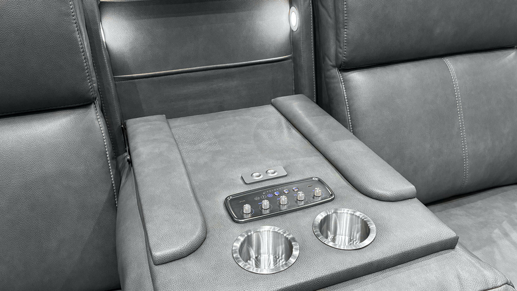 Close-up of a gray leather luxury vehicle interior center console with two cup holders, a control panel, and armrests.