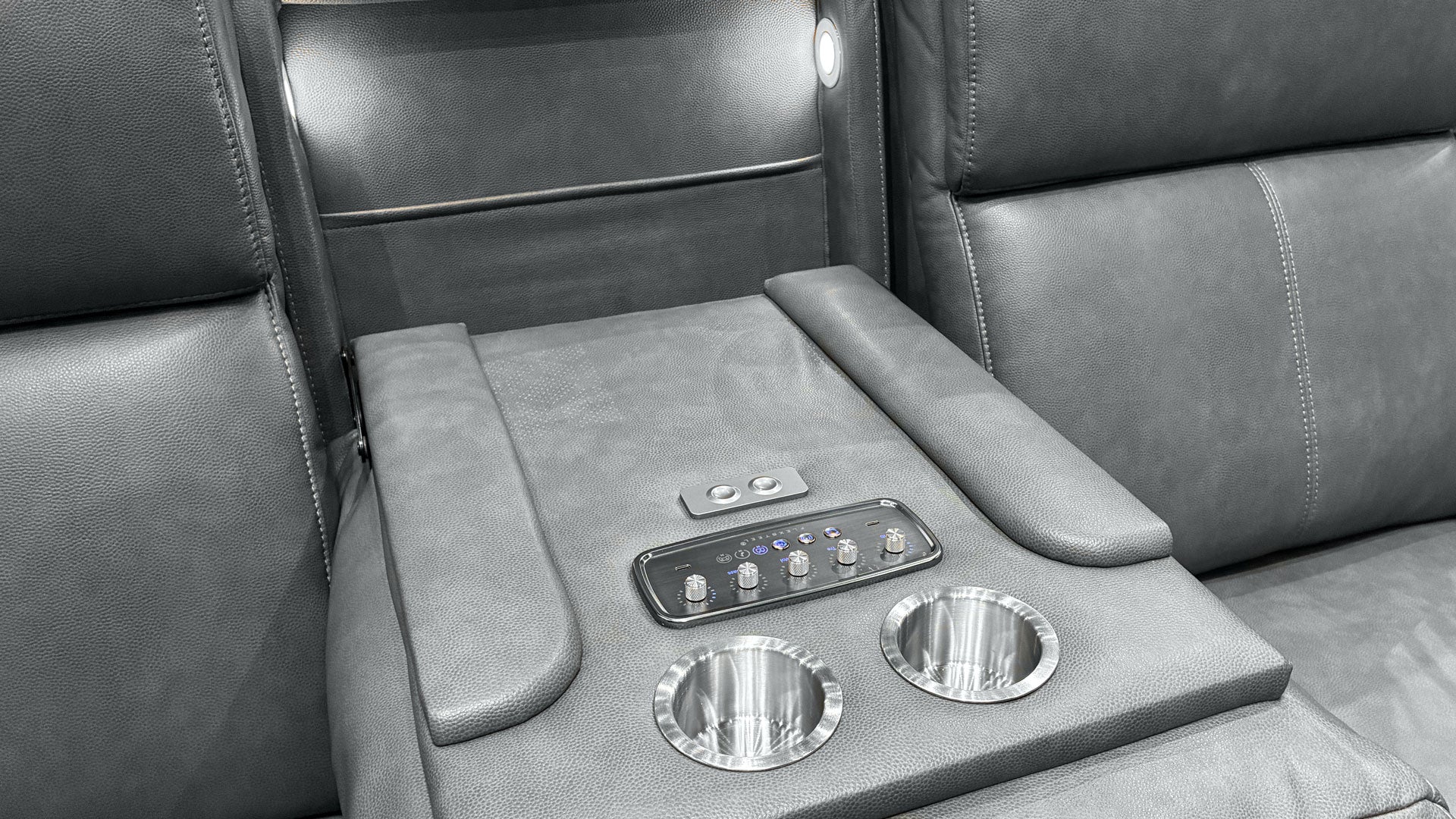 Close-up of a gray leather luxury vehicle interior center console with two cup holders, a control panel, and armrests.