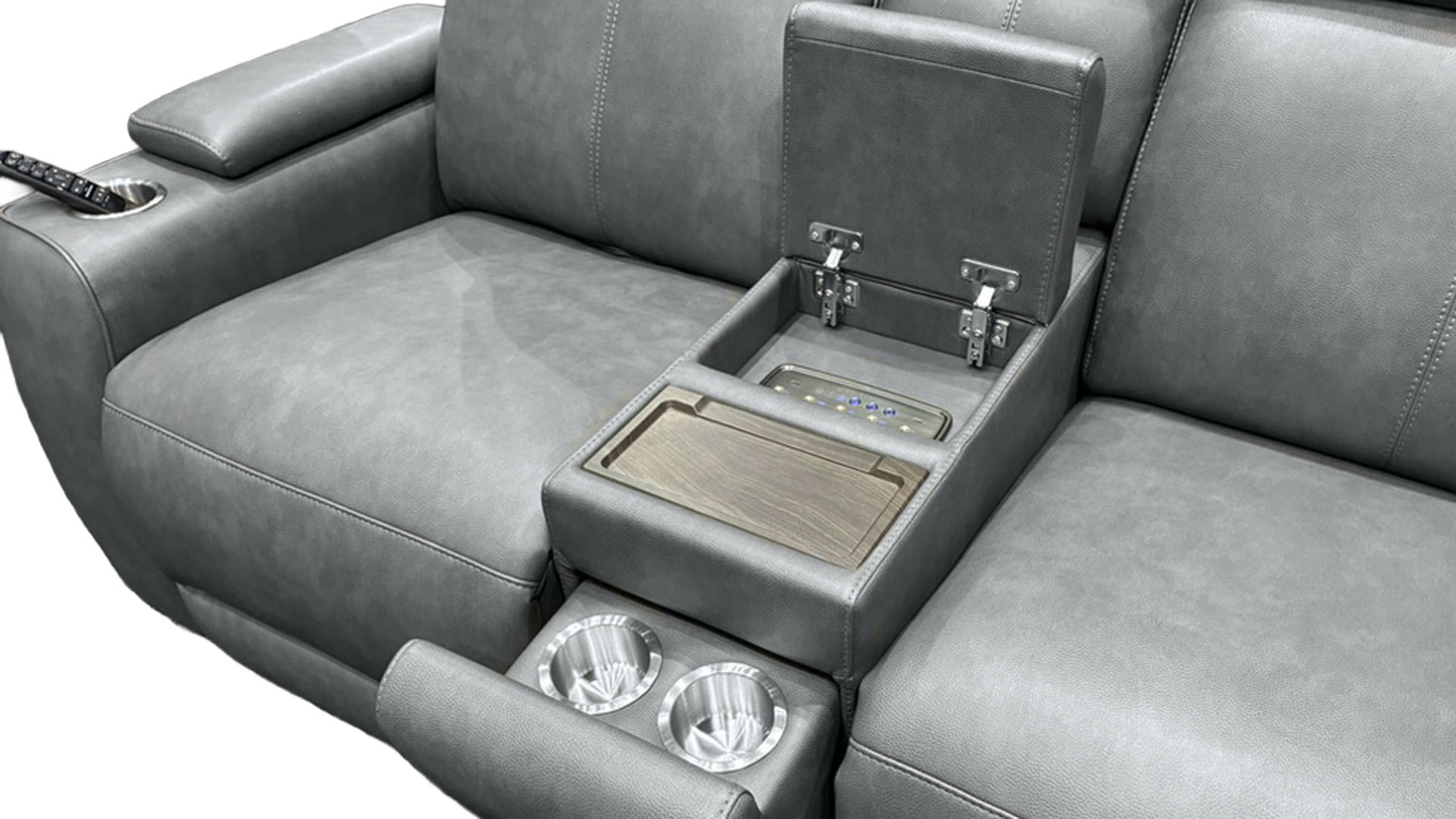 Gray leather reclining sofa with an open center console armrest showing a wood-look tray table, cup holders, and a control panel, photographed on a white background.