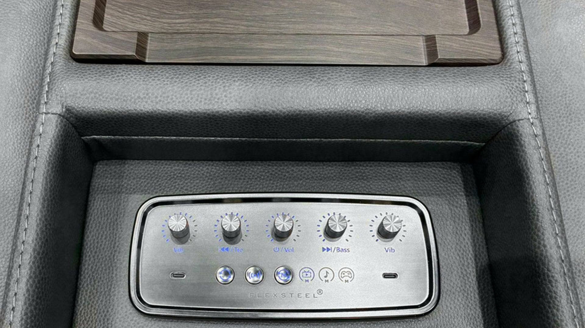Close-up of a car center console with a silver multi-zone climate control panel set into dark gray leather, below a wood-grain tray insert.