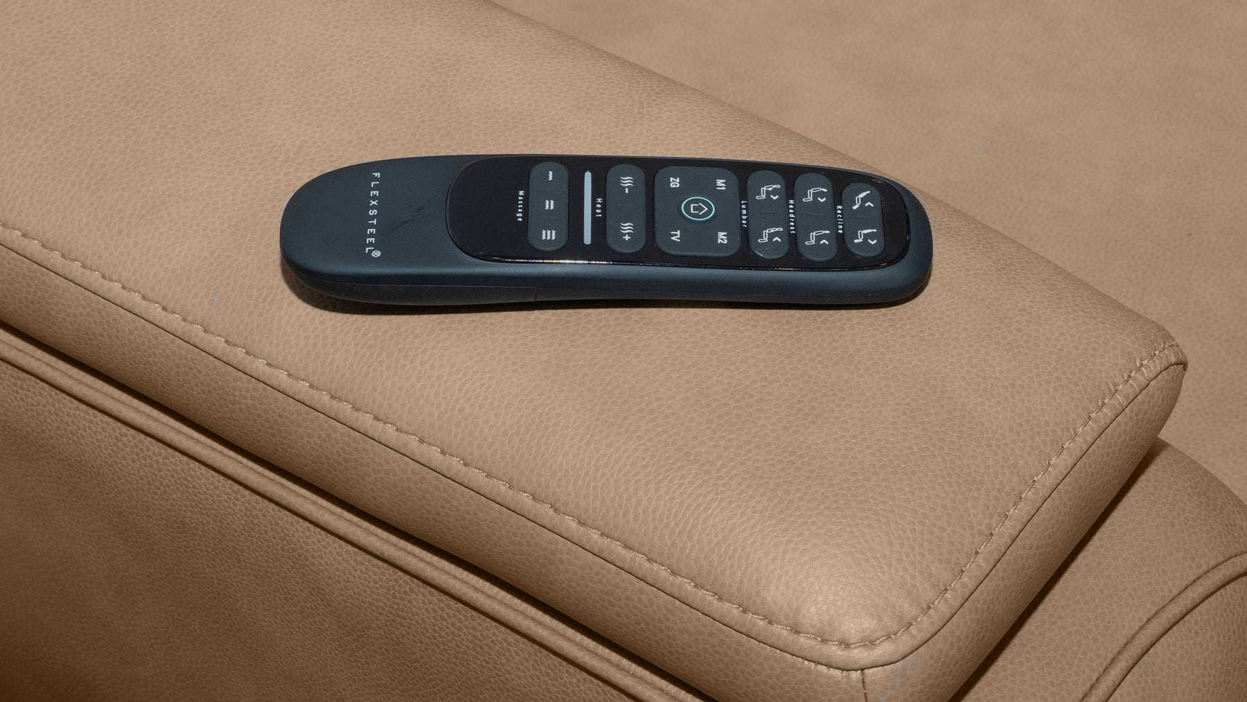 A dark gray Samsung smart remote control resting on the beige leather armrest of a modern chair.