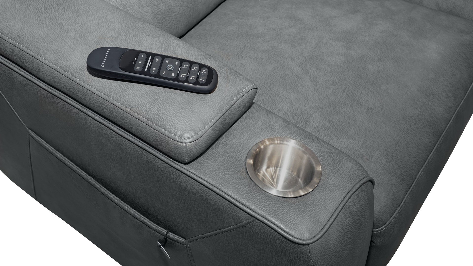 Close-up of a gray upholstered recliner chair showing the armrest with a black remote control resting on top and a circular metallic cup holder on the side.