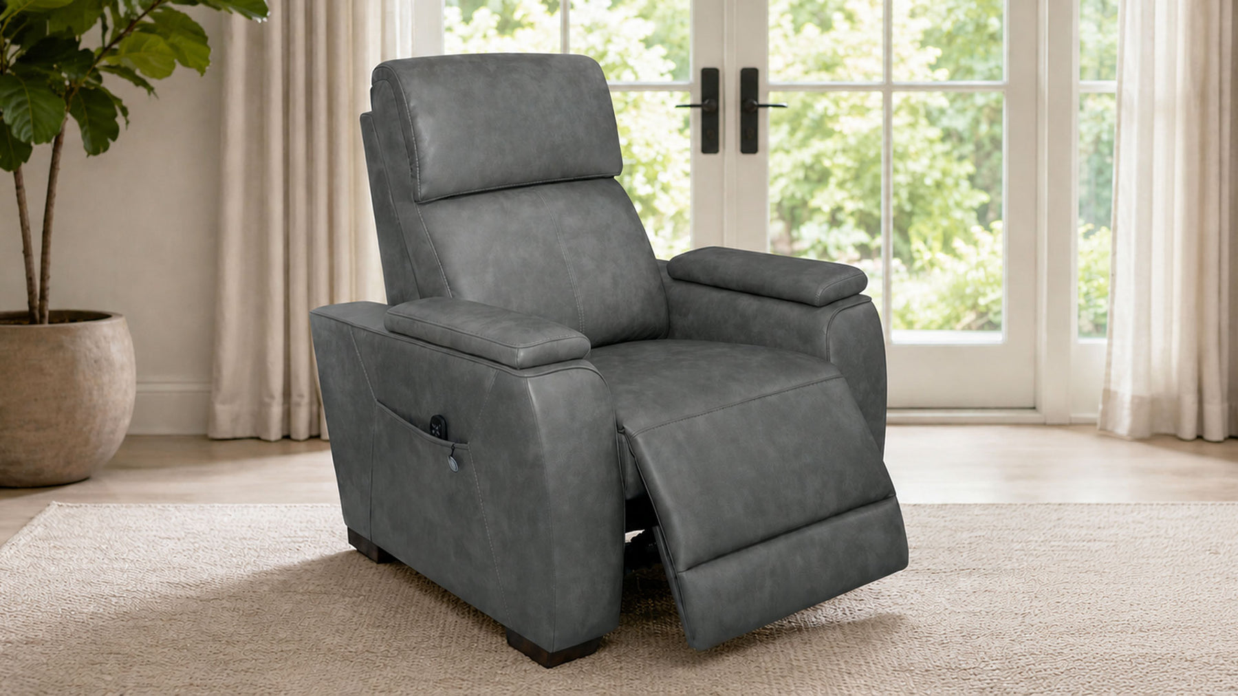 A gray upholstered recliner chair with the footrest extended, shown in a bright living room with large windows, curtains, and a potted plant.