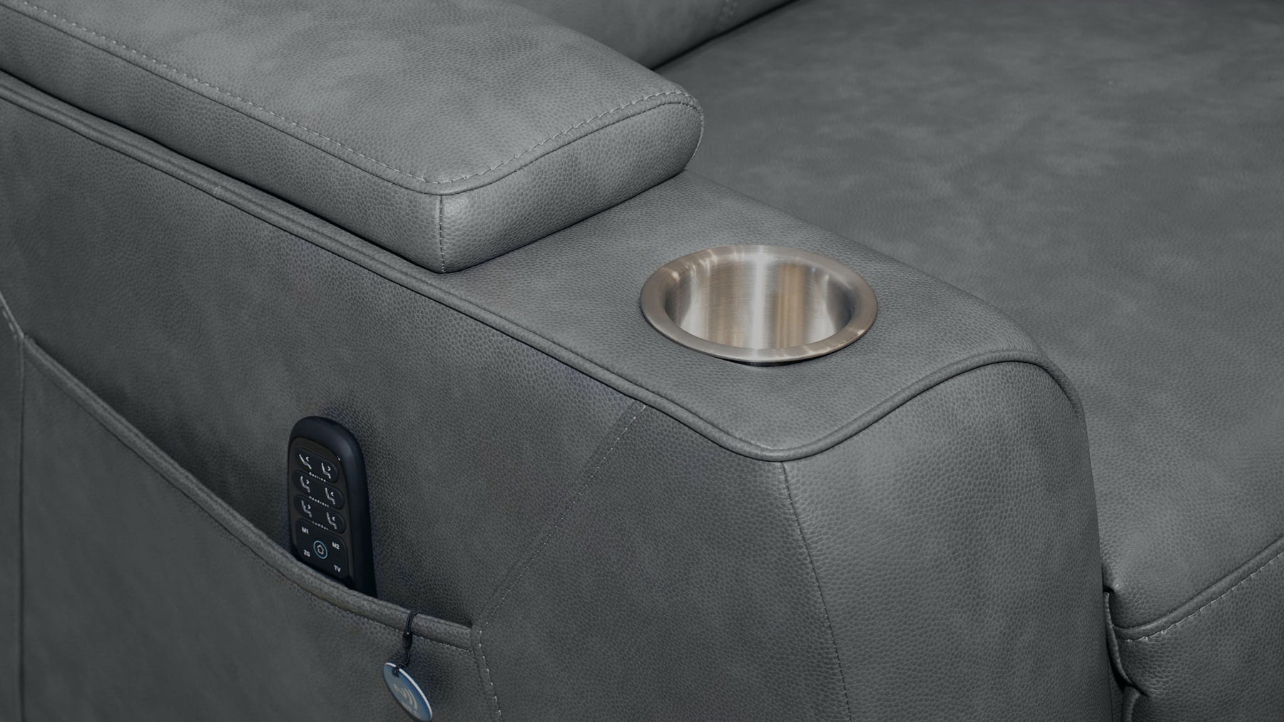 Close-up of a gray upholstered recliner arm with a circular metallic cup holder and a side pocket holding a remote control.