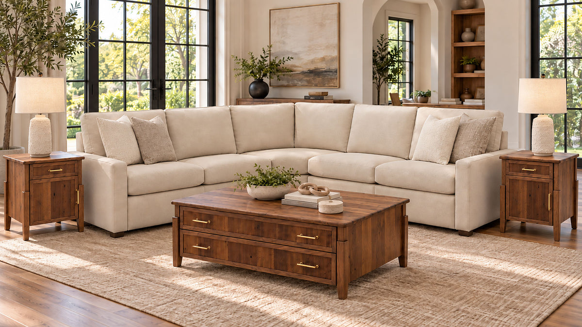 A staged living room scene showing a large cream sectional sofa with matching pillows, a dark wood coffee table, two matching wood side tables with white lamps, and a beige rug. No people or animals are present, but this is still a real interior environment rather than a clean studio product shot, so subject_type is Lifestyle.