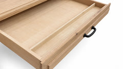 A close-up of a light natural wood drawer pulled open, showing a recessed interior divider and a black metal pull handle on a white background.