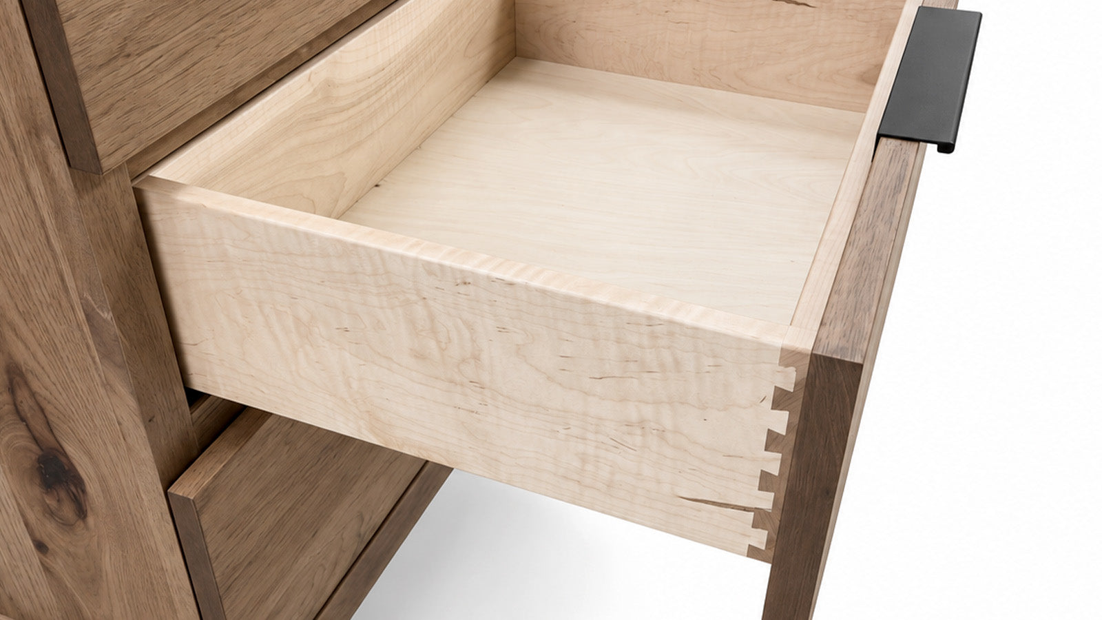Close-up of a wooden drawer pulled open, showing a light natural wood interior and dovetail joint construction, with a dark metal pull handle on a white background.