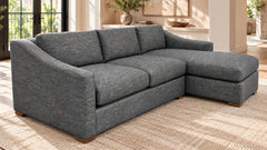A gray upholstered sectional sofa with a right-facing chaise lounge, shown in a bright, modern living room setting on a woven rug.