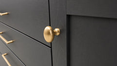 Close-up of a dark charcoal gray cabinet door with a round brushed gold pull knob, alongside matching gold drawer handles.