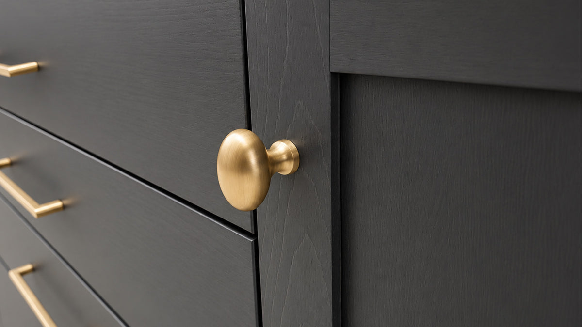 Close-up of a dark charcoal gray cabinet door with a round brushed gold pull knob, alongside matching gold drawer handles.