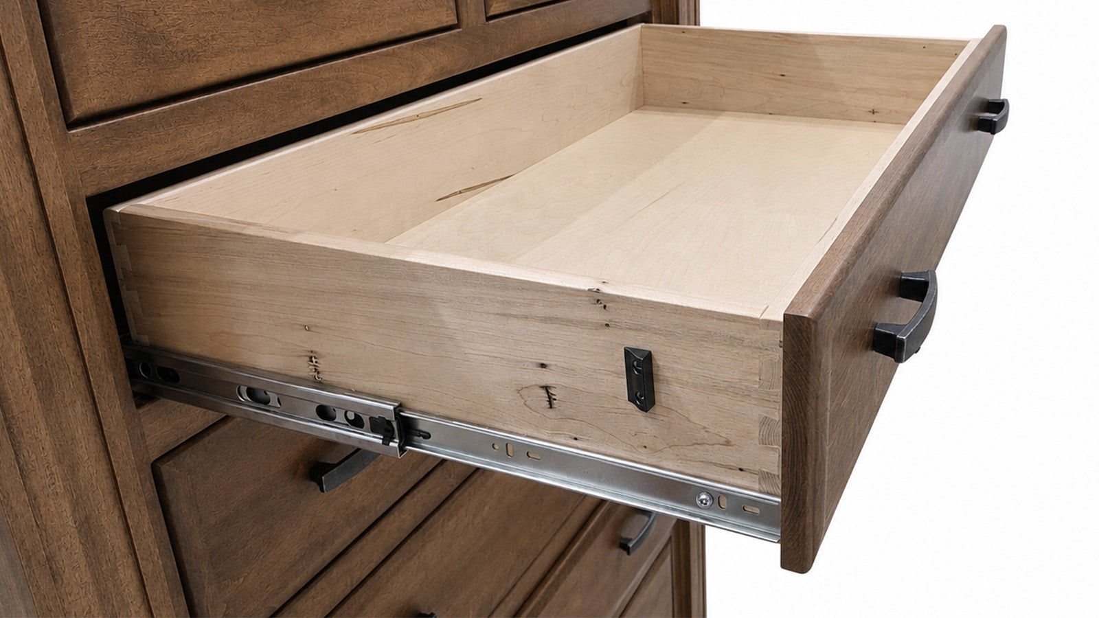 Un cajón de madera abierto, extraído de un armario de madera a juego, en el que se aprecia el veteado de la madera, las guías metálicas del cajón y los tiradores negros sobre un fondo blanco.