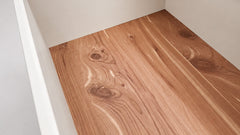 Light brown wood grain flooring planks installed on a floor inside a room with off-white walls.